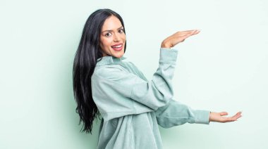 Güzel İspanyol kadın gülümsüyor, mutlu, pozitif ve tatmin olmuş hissediyor, fotokopi alanında nesne ya da konsept tutuyor ya da gösteriyor