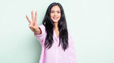 Güzel İspanyol kadın gülümsüyor ve arkadaş canlısı görünüyor. Üç ya da üç numarayı gösteriyor. Elleri önde, geriye doğru sayıyor.