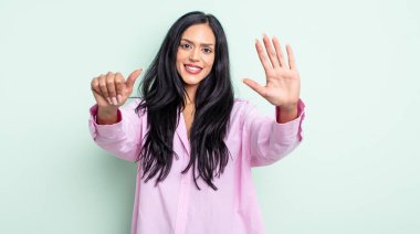 Güzel İspanyol bir kadın gülümsüyor ve arkadaş canlısı görünüyor, 6 ya da 6 numarayı gösteriyor, elleri önde, geriye doğru sayıyor.