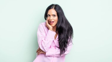 Güzel İspanyol bir kadın şok ve inançsızlık içinde, elleri yanağında ve kolları çaprazlanmış, sersemlemiş ve şaşırmış hissediyor.