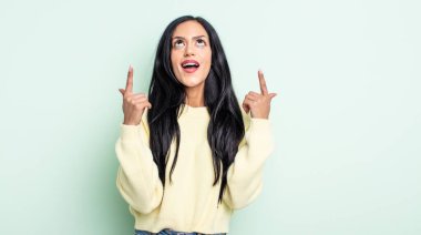 Güzel İspanyol kadın şaşırmış, şaşırmış ve ağzı açık görünüyor, iki eliyle boşluğu kopyalamak için yukarı bakıyor.