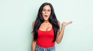 Güzel İspanyol kadın şaşırmış ve şok olmuş görünüyor, çenesi düşmüş, bir objeyi elinde açık bir elle tutuyor.