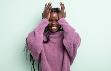 Siyah güzel bir kadın stresli ve endişeli, depresif ve hayal kırıklığına uğramış hissediyor, baş ağrısı ile iki elini de kafa kafaya kaldırıyor