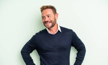 Orta yaşlı yakışıklı, mutlu, kendine güvenen, gururla gülümseyen ve iki elini de kalçasında görmek isteyen bir adam.