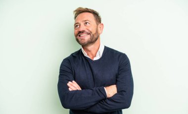 Orta yaşlı yakışıklı adam mutlu, gururlu ve umutlu merak ediyor ya da düşünüyor, çapraz kollarla fotokopi çekmeyi bekliyor.