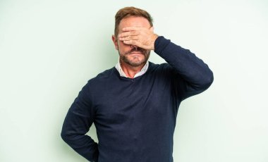 Orta yaşlı yakışıklı bir adam tek eliyle gözlerini kapatıyor korkmuş ya da endişeli hissediyor, merak ediyor ya da körü körüne bir sürpriz bekliyor.