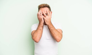 Orta yaşlı yakışıklı bir adam korkmuş ya da utanmış hissediyor. Gözleri yarı kapalı ya da elleri yarı kapalı bir şekilde dikizliyor.