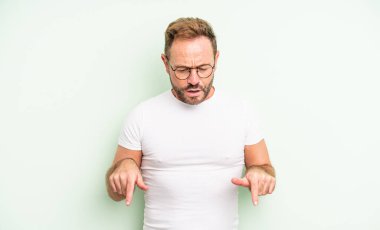 Orta yaşlı, ağzı açık, iki eliyle aşağıya bakan yakışıklı bir adam. Şaşırmış, şaşkın ve şaşırmış görünüyor.