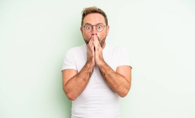 Orta yaşlı yakışıklı bir adam endişeli, üzgün ve korkmuş, elleri ağızda, endişeli ve berbat görünüyor.