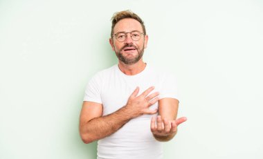 Orta yaşlı yakışıklı bir adam mutlu ve aşık, bir eli kalbinin yanında gülümsüyor ve diğer eli önde uzanıyor.