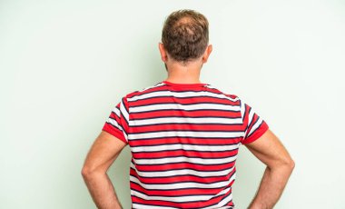 Orta yaşlı yakışıklı bir adam kafası karışık ya da dolu ya da şüphe ve soru dolu, merak ediyor, elleri kalçasında, dikiz aynasından