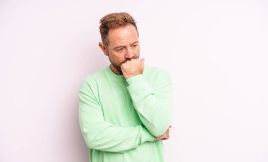 Orta yaşlı yakışıklı bir adam ciddi, düşünceli ve endişeli, elleri çenesine bastırılmış bir şekilde yan bakıyor.