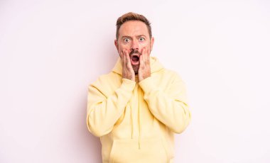 Orta yaşlı yakışıklı adam şok olmuş ve korkmuş hissediyor, ağzı açık ve elleri yanaklarında korkmuş görünüyor.