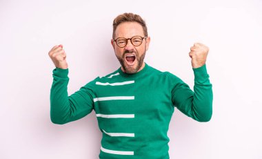 Orta yaşlı yakışıklı bir adam sinirli bir ifadeyle agresif bir şekilde bağırıyor ya da yumruklarıyla başarıyı kutluyor.