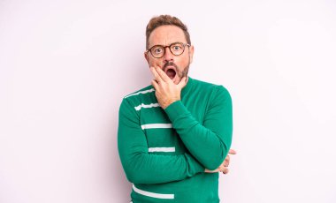 Orta yaşlı, ağzı ve gözleri açık ve eli çenesinde olan yakışıklı bir adam. Hoş olmayan bir şok geçiriyor.