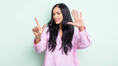 Güzel İspanyol bir kadın gülümsüyor ve dost canlısı görünüyor, 7 ya da 7 numarayı gösteriyor, eli önde, geriye doğru sayıyor.