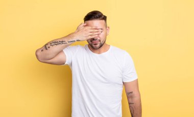 Genç yakışıklı bir adam tek eliyle gözlerini kapatıyor. Korkmuş ya da endişeli, merak ediyor ya da körü körüne bir sürpriz bekliyor.