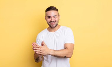 Genç yakışıklı adam kendini mutlu ve başarılı hissediyor, gülümsüyor ve alkışlıyor, alkışlarla tebrik ediyor.