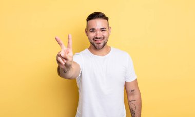 Genç yakışıklı adam gülümsüyor ve arkadaş canlısı görünüyor, iki ya da iki numarayı gösteriyor, elleri önde, geriye doğru sayıyor.