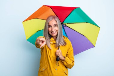 Orta yaşlı beyaz saçlı kadın kamerayı işaret ederek seni seçiyor. şemsiye ve yağmur kavramı