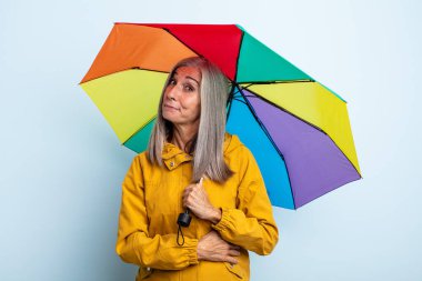 Orta yaşlı beyaz saçlı kadın omuz silkiyor, kafası karışık ve kararsız hissediyor. şemsiye ve yağmur kavramı
