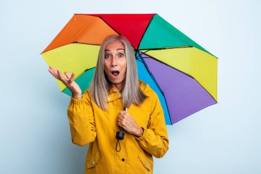 Orta yaşlı beyaz saçlı kadın inanılmaz bir sürprizle şaşkına dönmüş ve hayrete düşmüştü. şemsiye ve yağmur kavramı