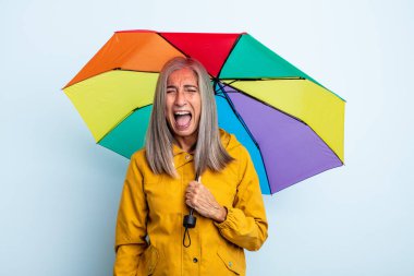 Orta yaşlı, gri saçlı kadın agresif bir şekilde bağırıyor, çok kızgın görünüyor. şemsiye ve yağmur kavramı