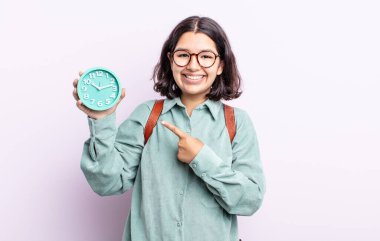 Güzel, genç bir bayan neşeyle gülümsüyor, mutlu hissediyor ve bir tarafı işaret ediyor. Alarm saati kavramı