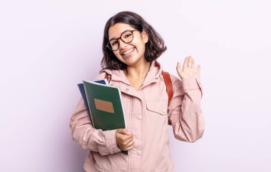 Güzel, genç bir bayan mutlu bir şekilde gülümsüyor, el sallıyor, sizi selamlıyor ve selamlıyor. Kitap konsepti olan öğrenci
