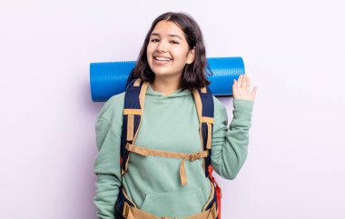 Güzel, genç bir bayan mutlu bir şekilde gülümsüyor, el sallıyor, sizi selamlıyor ve selamlıyor. yürüyüş kavramı