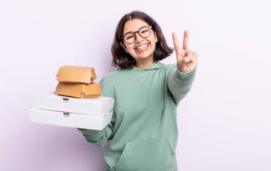 Gülümseyen ve mutlu görünen güzel genç bir kadın zafer ya da barış işareti yapıyor. Fast food konsepti.