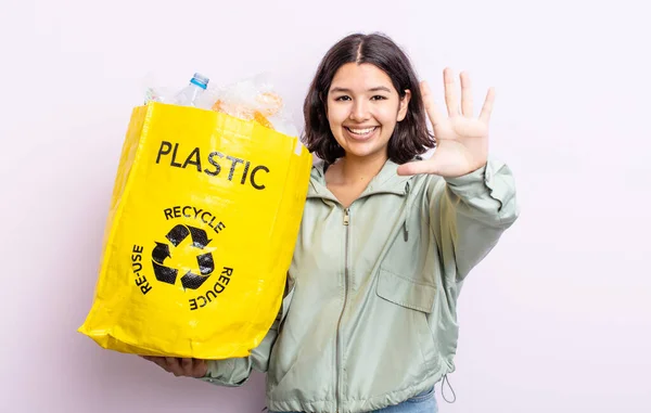 かなり若い女性は笑顔で友好的に見える5番目を示しています プラスチックリサイクルの概念 — ストック写真