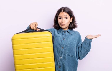 Güzel genç bir kadın şaşkın, şaşkın ve şüpheci hissediyor. seyahat çantası kavramı