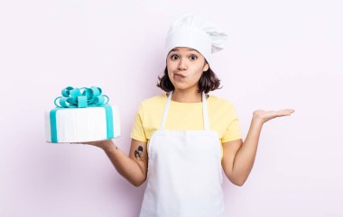 Güzel genç bir kadın şaşkın, şaşkın ve şüpheci hissediyor. Şef kek pişiriyor.