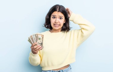 Güzel genç bir kadın stresli, endişeli ya da korkmuş hissediyor. Elleri başının üstünde. Dolar banknotları konsepti