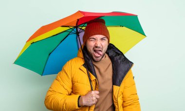 Genç, yakışıklı, neşeli ve asi tavırlı, şaka yapan ve dilini dışarı çıkaran bir adam. yağmur ve şemsiye kavramı