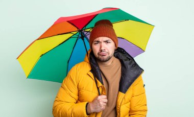 Genç ve yakışıklı bir adam üzgün ve mızmızlanıyor. Mutsuz bir bakışı var ve ağlıyor. yağmur ve şemsiye kavramı