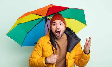 Genç ve yakışıklı bir adam şok olmuş ve şaşırmış hissediyor. yağmur ve şemsiye kavramı