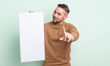 Genç yakışıklı adam gururla gülümsüyor ve kendinden emin bir numara oluyor. boş tuval kavramı