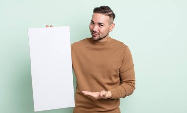 young handsome man smiling cheerfully, feeling happy and showing a concept. empty canvas concept