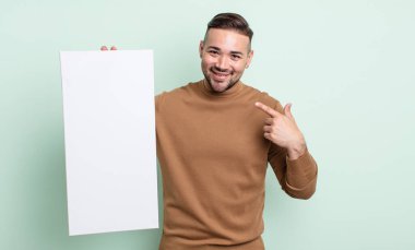 young handsome man smiling confidently pointing to own broad smile. empty canvas concept