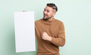 young handsome man feeling happy and facing a challenge or celebrating. empty canvas concept