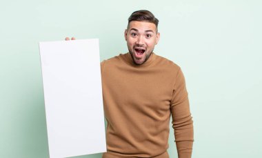 young handsome man looking happy and pleasantly surprised. empty canvas concept
