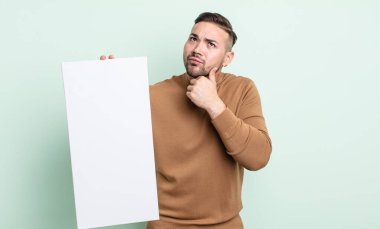 young handsome man thinking, feeling doubtful and confused. empty canvas concept