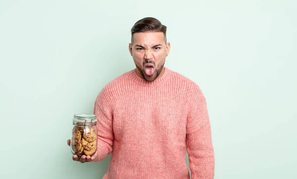 若いハンサムな男はうんざりしていらいらして舌を出す クッキーボトルのコンセプト — ストック写真