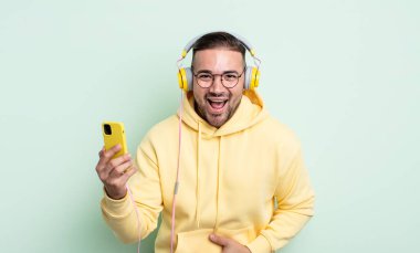 Genç yakışıklı bir adam komik bir şakaya yüksek sesle gülüyor. kulaklıklar ve akıllı telefon konsepti