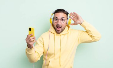 Genç ve yakışıklı bir adam stresli, endişeli ya da korkmuş hissediyor. Elleri başının üstünde. kulaklıklar ve akıllı telefon konsepti