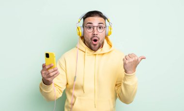 İnanamadığı için şaşırmış genç ve yakışıklı bir adam. kulaklıklar ve akıllı telefon konsepti