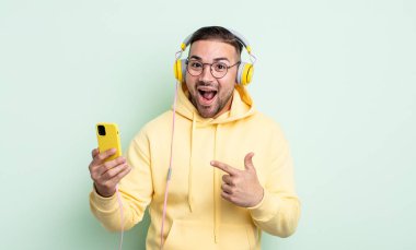 Genç yakışıklı adam heyecanlı ve şaşırmış görünüyor. kulaklıklar ve akıllı telefon konsepti