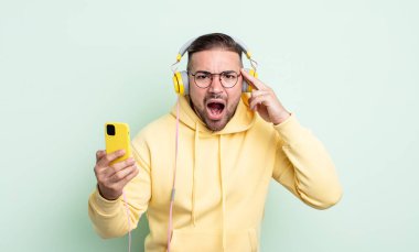 Genç yakışıklı adam şaşırmış görünüyor, yeni bir düşünce, fikir ya da konsept fark ediyor. kulaklıklar ve akıllı telefon konsepti